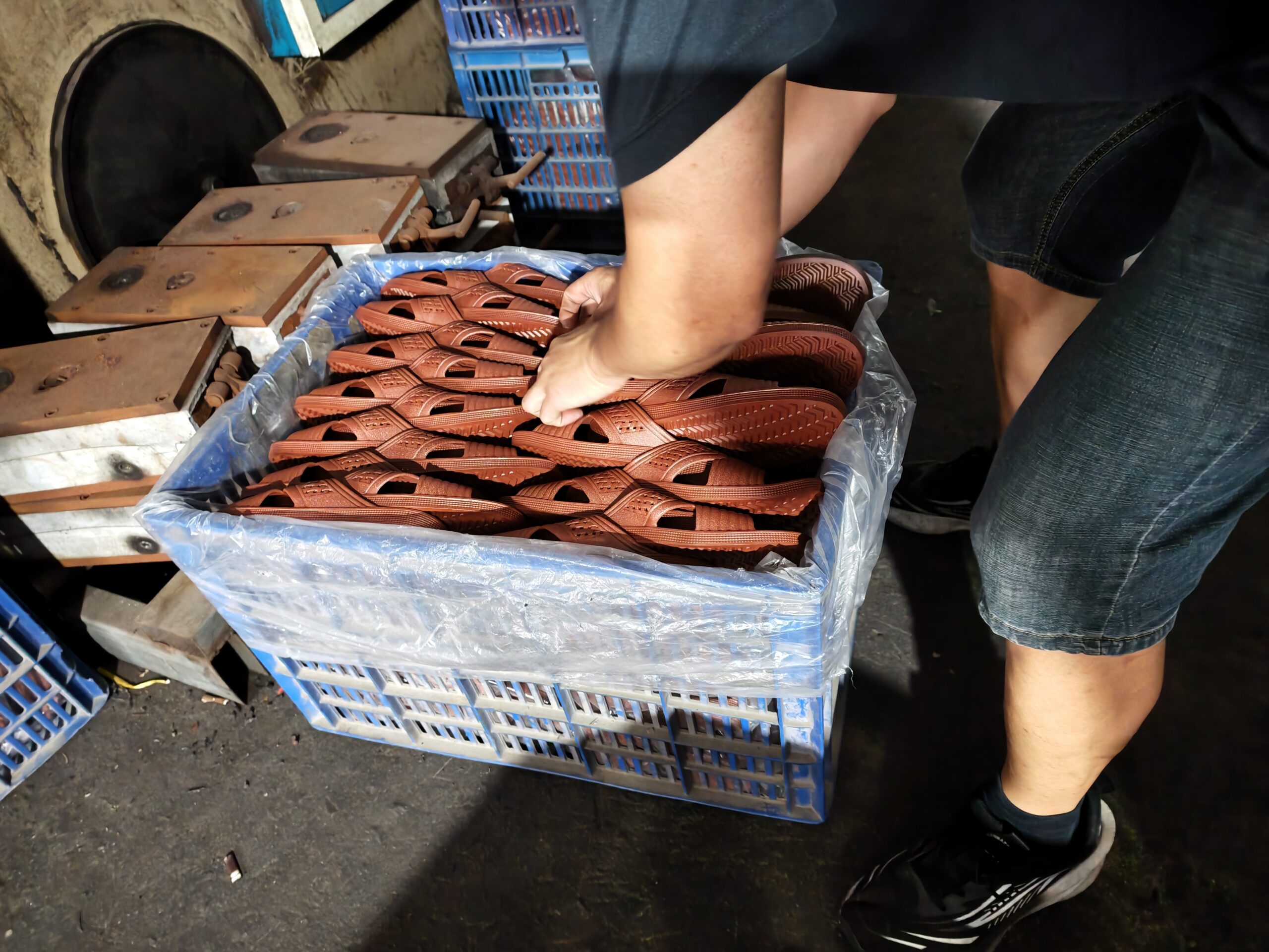 Worker arranging molded sandals in a storage crate at a footwear workshop.